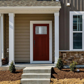 Red entry door on a house porch, with white decorative frame around the upper glass panel and white columns.