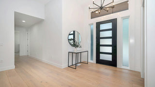 	Modern interior entryway with light wood floors, a black door with horizontal glass panels, and a round mirror.