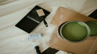 Overhead view of a can of green paint, a roller, a brush, and a paint tray on a drop cloth.